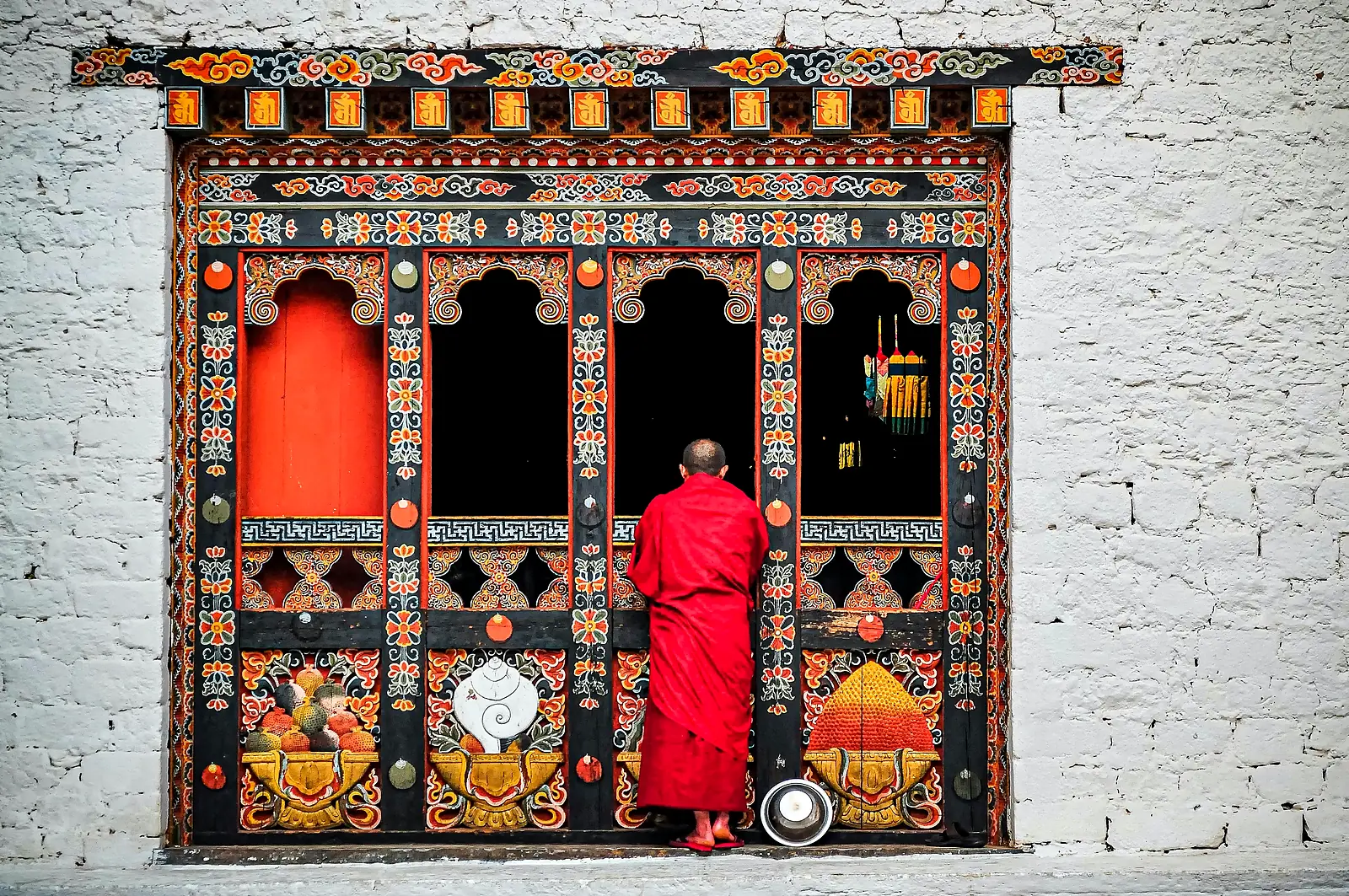 A monk in red robes at a painted temple window, Bhutan