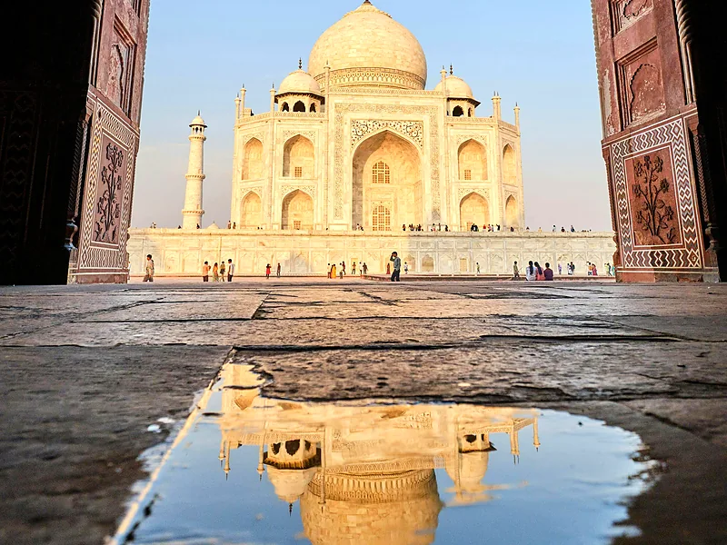 The Taj Mahal framed by a red sandstone arch and reflected in a pool